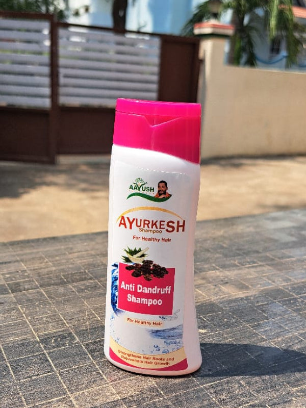 A bottle of Ayur Ashrama Anti-Dandruff Shampoo placed on a surface with a blurred background.